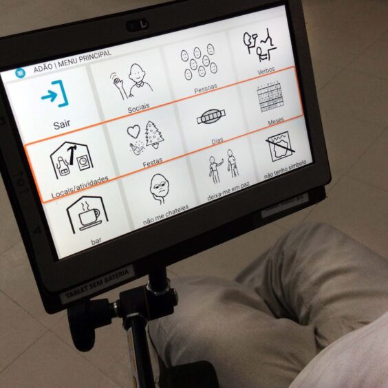 Tablet em suporte de cadeira de rodas. São visíveis as pernas de alguém que usa a cadeira. No tablet são visíveis várias imagens e um total de 12 conceitos.