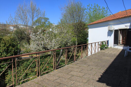 Imagem de um terraço. Vê-se parte de um edifício e inúmeras árvores ao fundo.