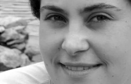 Fotografia, de rosto, em tons cinza. Aparece uma pessoa sorridente em grande plano.