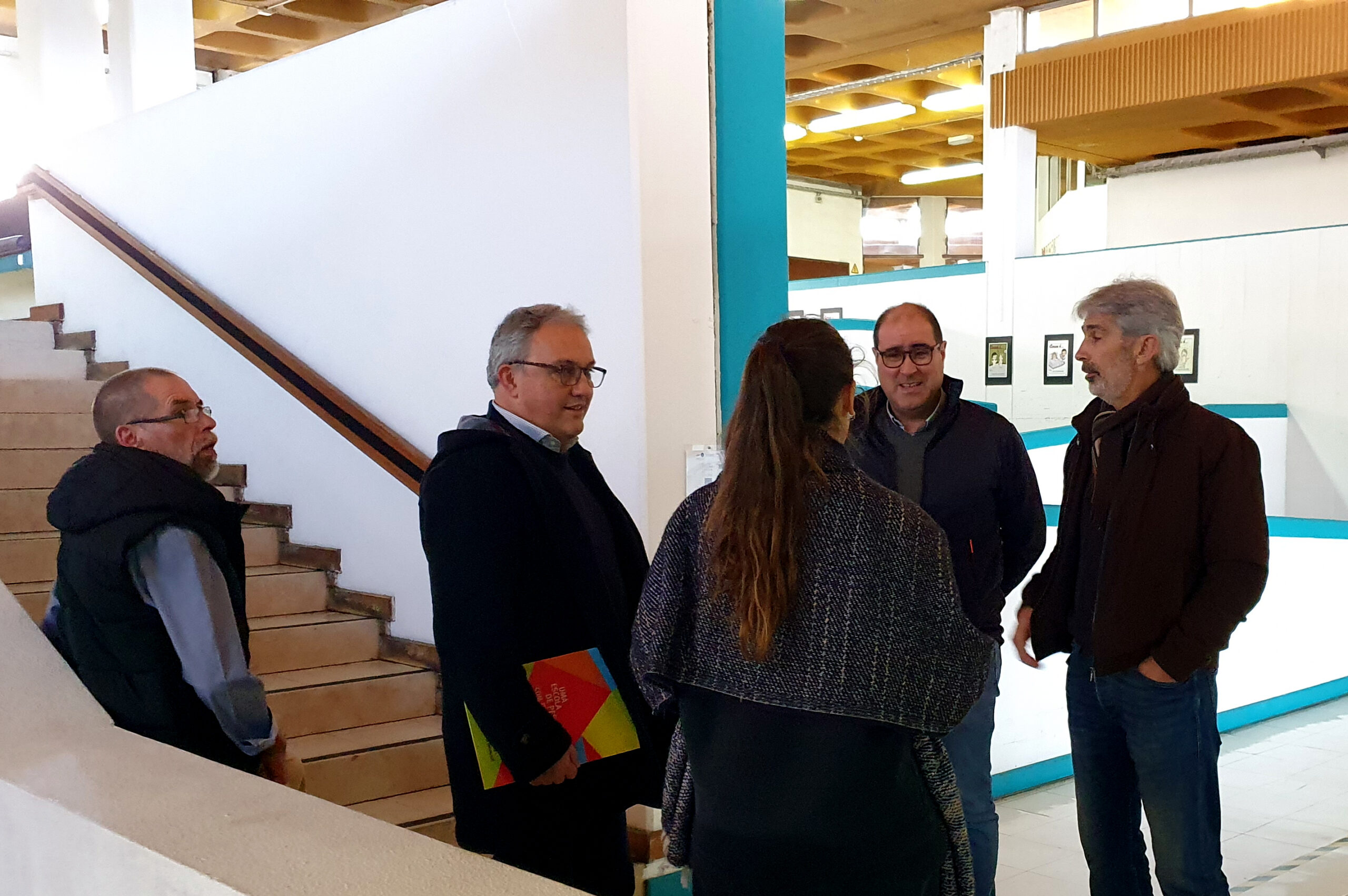 Cinco pessoas, em conversa, junto de escadas e rampa interna de acesso no Centro de Reabilitação.