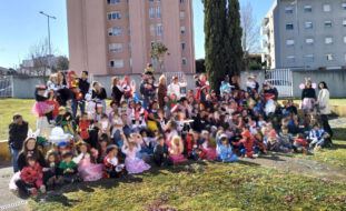 Fotografia de grupo, em jardim, com várias dezenas de crianças (e adultos) devidamente mascaradas. Ao fundo estão dois edifícios habitacionais. Os rostos das crianças estão desfocados.