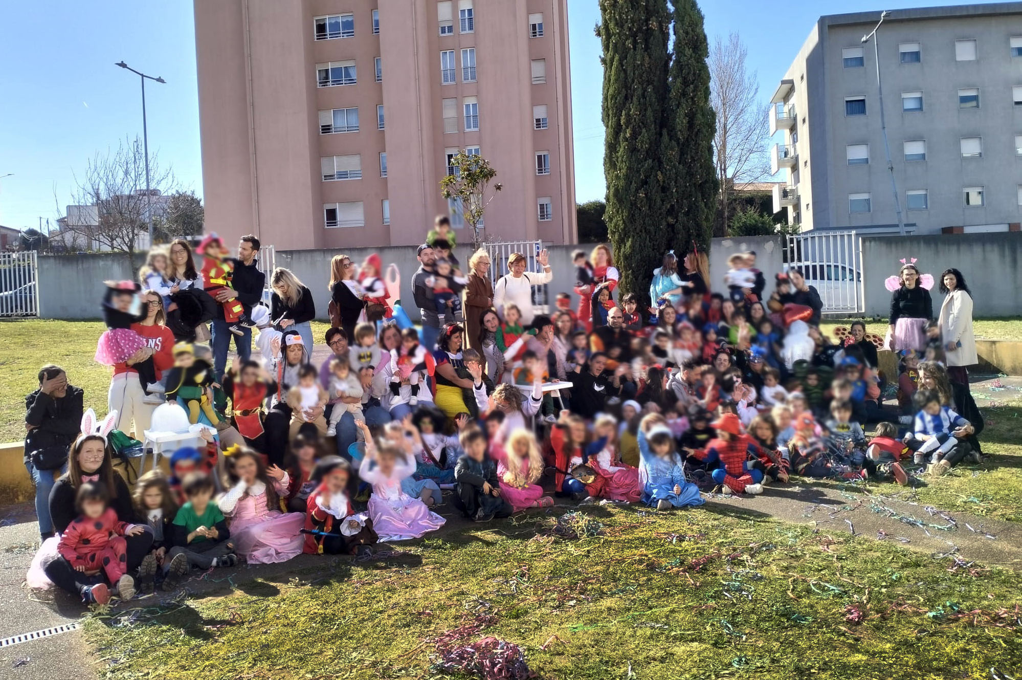 Fotografia de grupo, em jardim, com várias dezenas de crianças (e adultos) devidamente mascaradas. Ao fundo estão dois edifícios habitacionais. Os rostos das crianças estão desfocados.