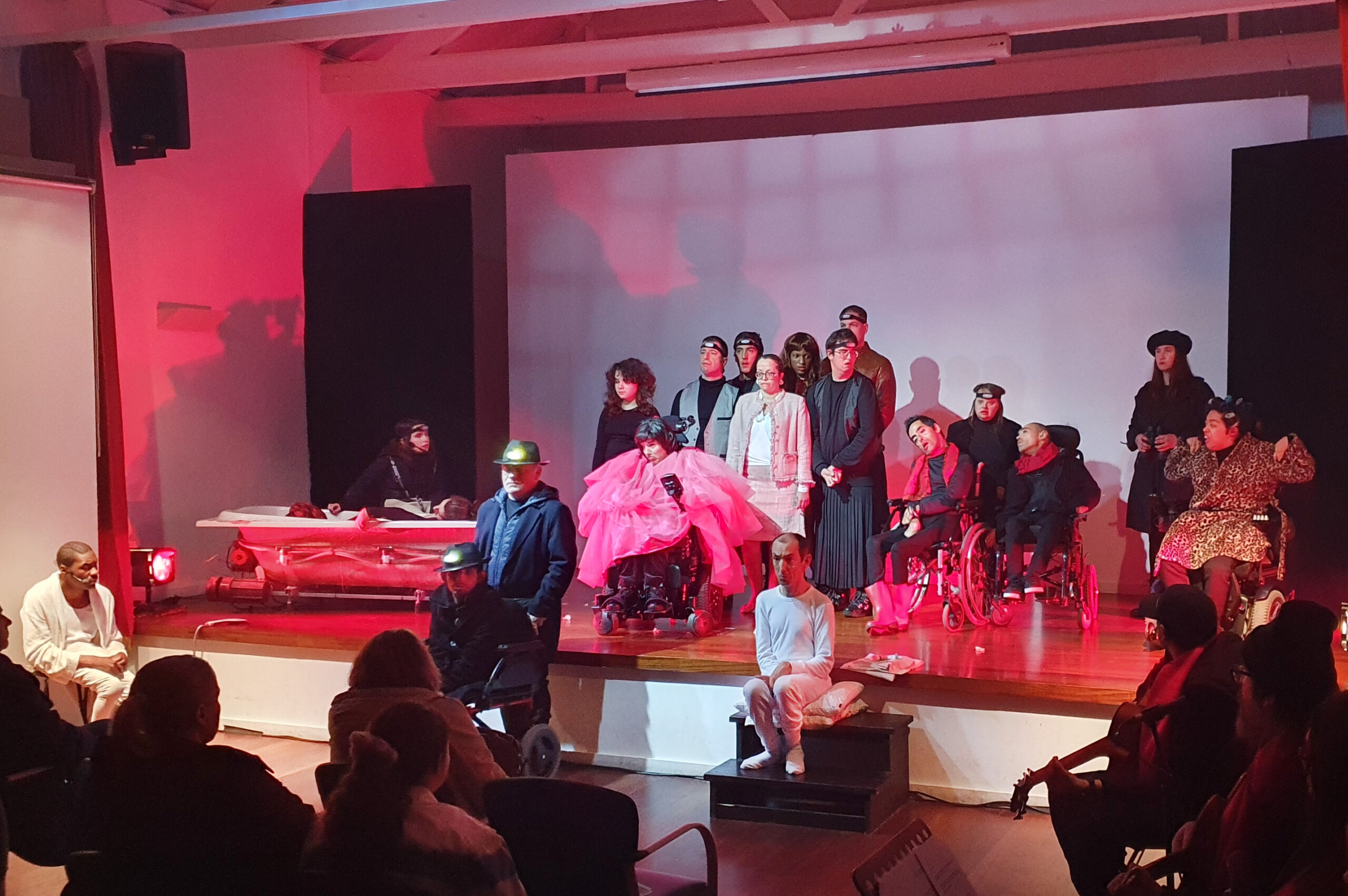 Fotografia de 19 atores e atrizes em palco, já na fase final da peça. À direita conseguem-se ainda ver alguns dos elementos da banda que atuou ao vivo.
