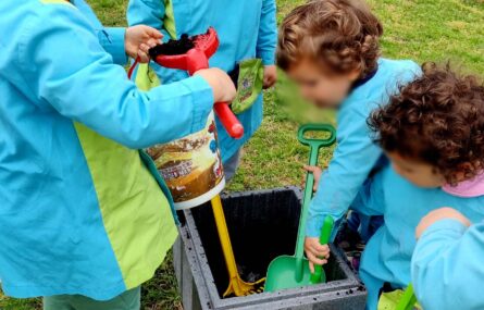 Cinco crianças brincam no jardim a mexer em terra. Todos os rostos das crianças aparecem desfocados