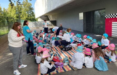 Sentadas em várias mantas estão várias dezenas de crianças a preparam-se para lanchar. Alguns adultos ajudam. Todos os rostos das crianças aparecem desfocados.
