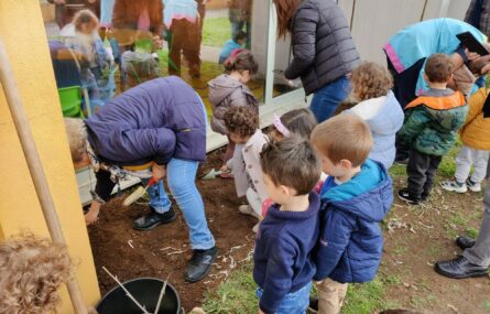 Um grupo de crianças está a fazer jardinagem. Estão acompanhadas por alguns adultos. Todos os rostos das crianças aparecem desfocados.