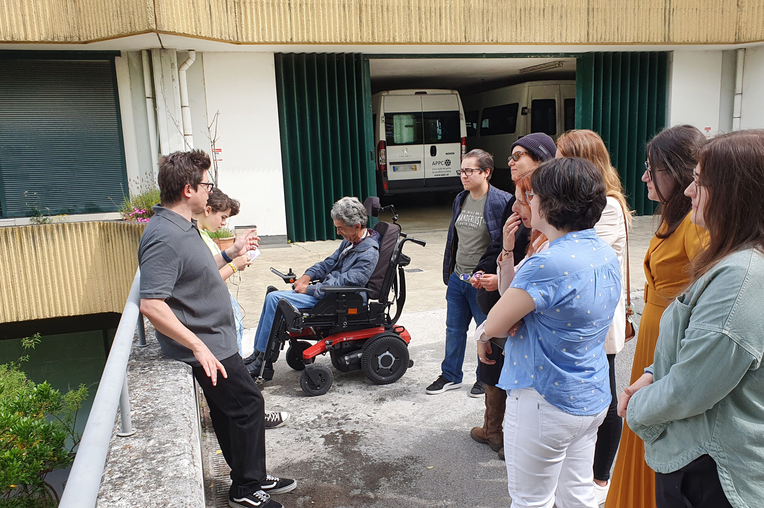 Pessoas à conversa em espaço exterior da Unidade Residencial “Villa Urbana”. Ao fundo encontram-se estacionadas duas das viaturas da APPC