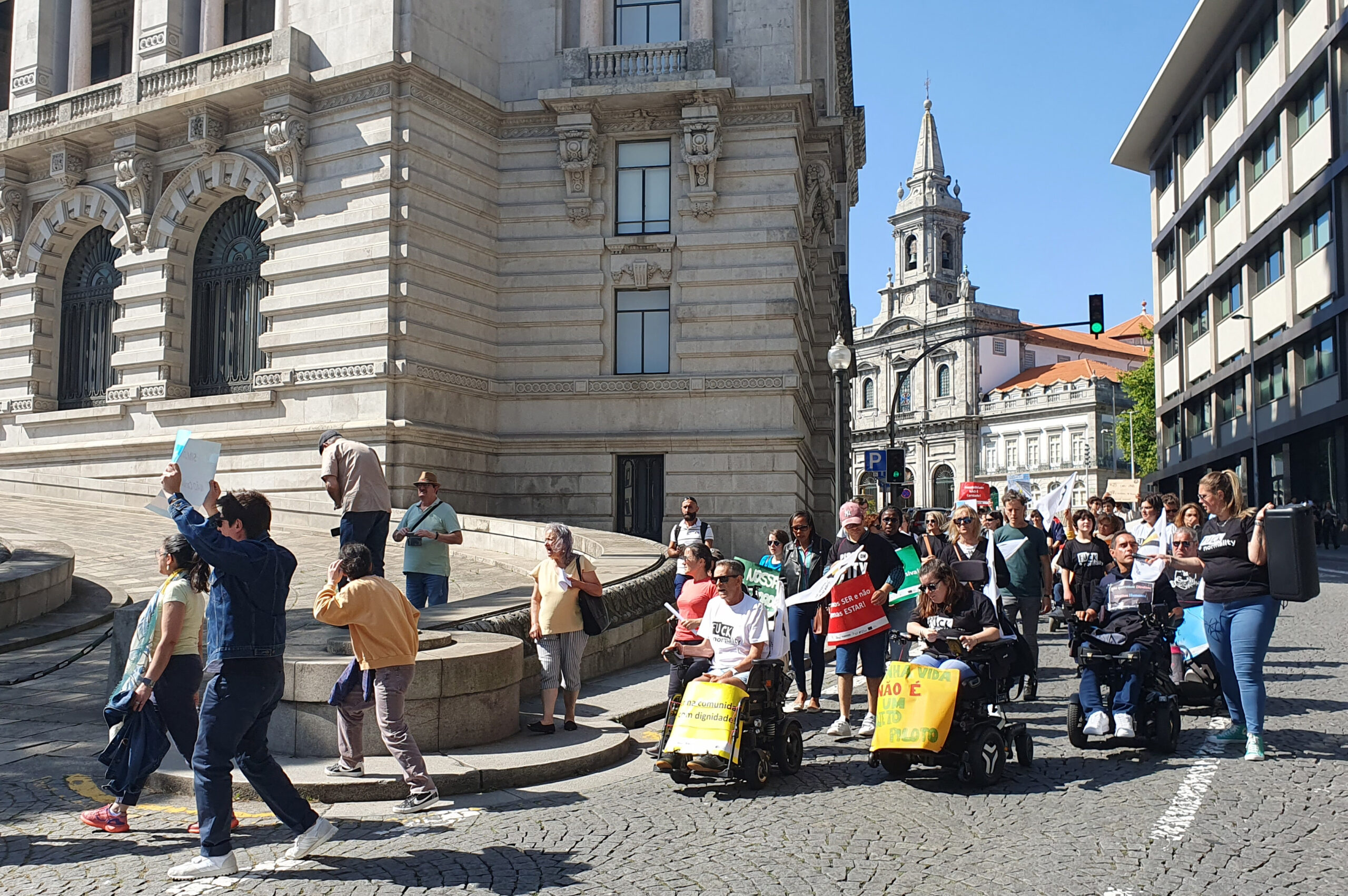 Aspeto parcial da Marcha. À frente uma pessoa empunha um cartaz com frase que é ilegível. Mais atrás outro manifestante usa megafone e coluna para dizer palavras de ordem.