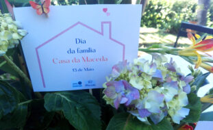 Imagem de cartaz alusivo ao Dia da Família. O cartaz está colocado junto de vasos com flores.