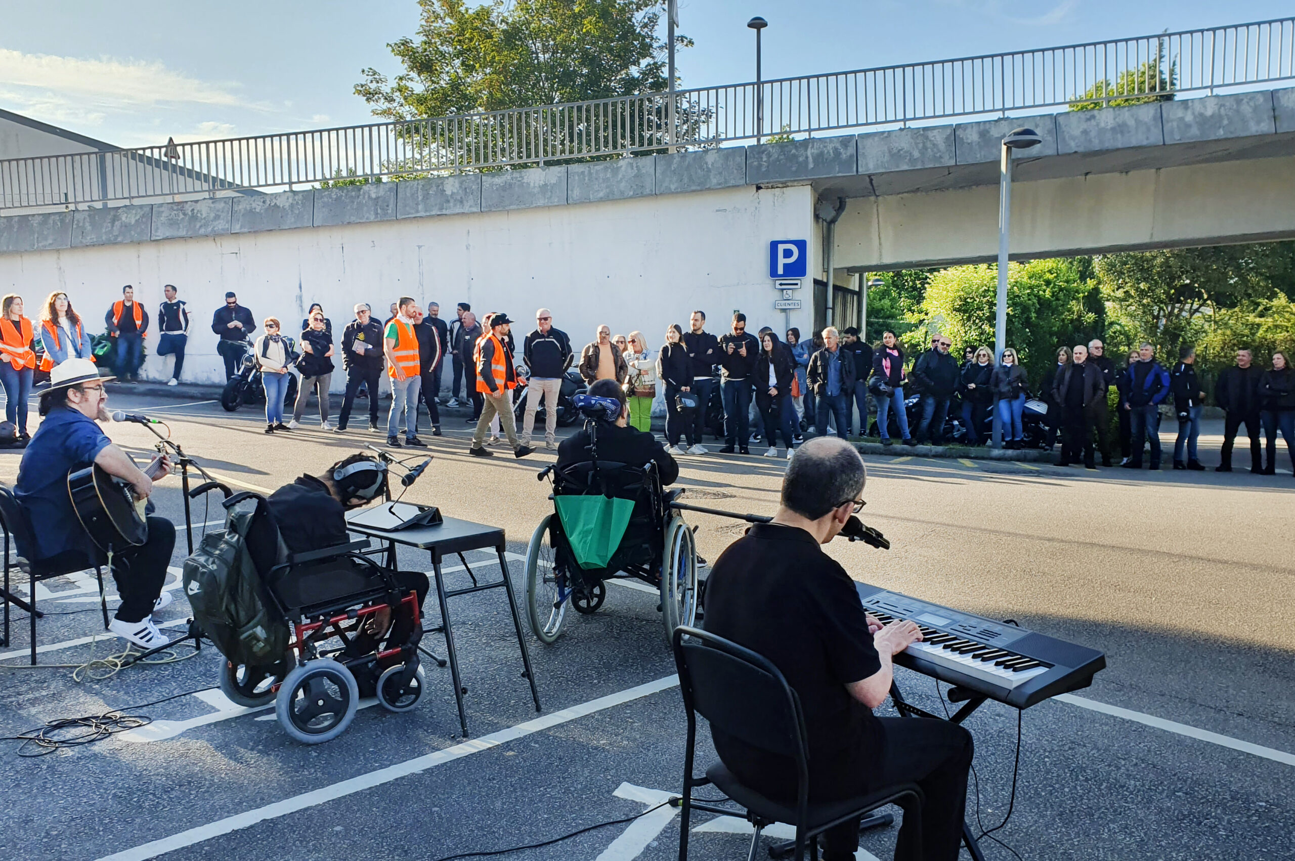 De costas estão os elementos da banda appSound enquanto atuam. Ao fundo várias dezenas de pessoas assistem ao concerto.