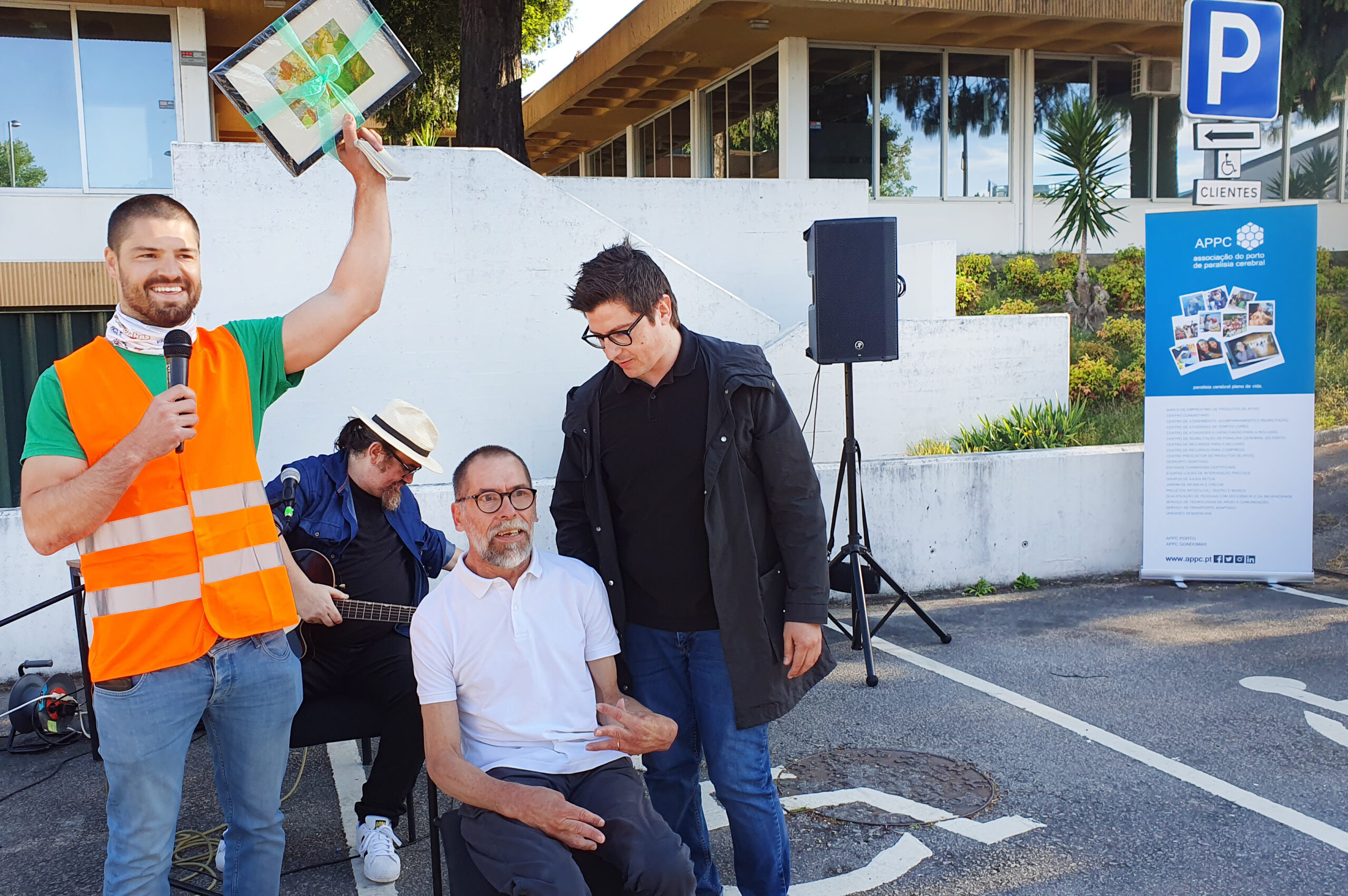Quatro pessoas na imagem. Uma, com colete laranja, sorri e levanta um quadro. Ao lado um dos elementos da banda appSound e dois representantes da Direção da APPC.