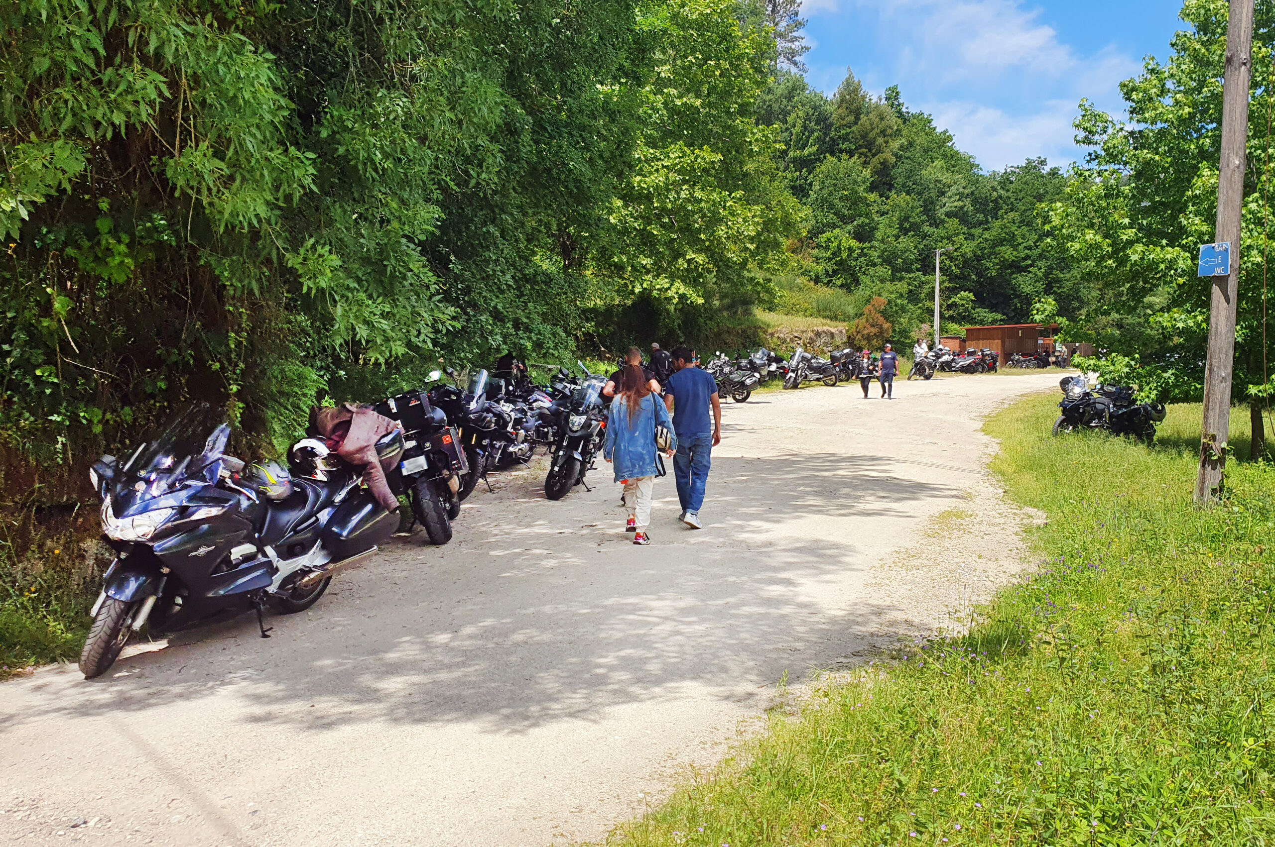 Aspeto parcial de zona do parque onde ficaram estacionadas várias dezenas de motos. Algumas pessoas estão a passear e a apreciar a paisagem e as motos.