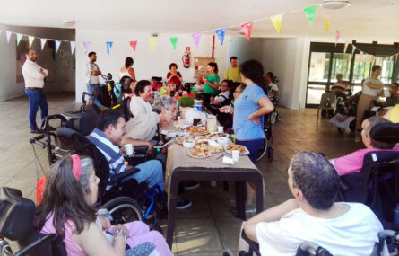 Mais de duas dezenas de pessoas em convívio junto de várias mesas com comidas e bebidas.