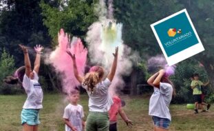 Imagem de divulgação de Voluntariado para acompanhamento nas atividades de verão (em julho, agosto e setembro) do Centro de Atividades de Tempos Livres. Fotografia de cinco crianças em jardim a lançarem pó colorido para o ar. Ao fundo, junto das árvores, estão mais duas crianças. Na parte superior da imagem, uma abelha, um coração encarnado e um losango a comporem o símbolo do Voluntariado da APPC. Em baixo, em letras brancas sobre fundo azul, a frase “Comprometa-se com uma causa”, a indicação do sítio da APPC e as respetivas redes sociais.