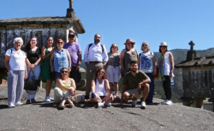 Fotografia de 13 pessoas junto de espigueiros do Soajo. Ao fundo, montes e céu azul.