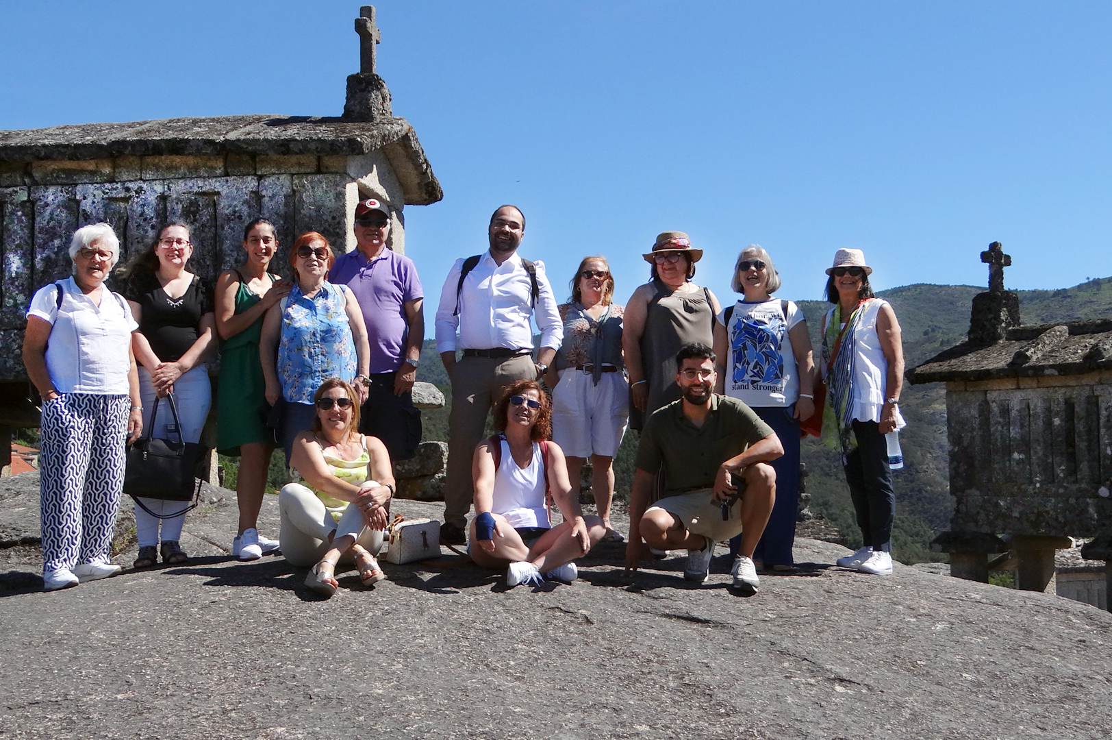 Fotografia de 13 pessoas junto de espigueiros do Soajo. Ao fundo, montes e céu azul.