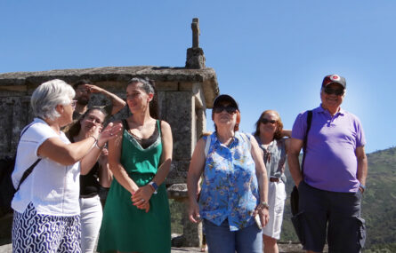 Grupo de sete pessoas – todas sorridentes – junto de um dos espigueiros do Soajo. Ao fundo, montes e céu azul.