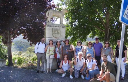 Fotografia de grupo, com 13 pessoas, junto de escultura de homenagem ao Cão Sabujo da Serra do Soajo. Em primeiro plano um sinal de trânsito tapa parcialmente a pessoa mais à direita. Ao fundo, árvores e montes em paisagem.