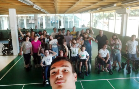 Selfie de grupo de pessoas em espaço interior do Centro de Reabilitação da APPC. Em primeiro plano rosto de quem fez a fotografia. Mais atrás perto de três dezenas de pessoas acenam para a fotografia.