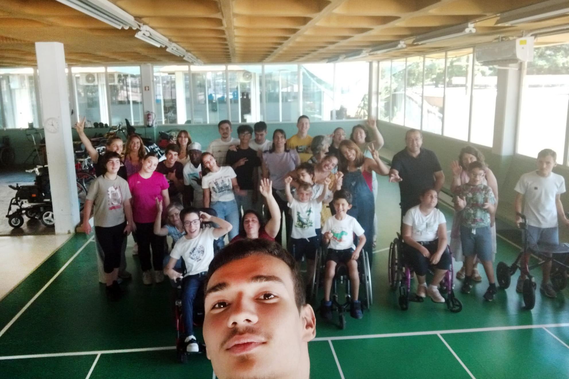 Selfie de grupo de pessoas em espaço interior do Centro de Reabilitação da APPC. Em primeiro plano rosto de quem fez a fotografia. Mais atrás perto de três dezenas de pessoas acenam para a fotografia.