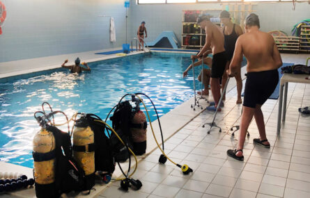 Fotografia da piscina da Villa Urbana de Valbom. Dentro da piscina está já uma pessoa. Preparam-se outras cinco para entrar na água. Em primeiro plano botijas e equipamento de mergulho.