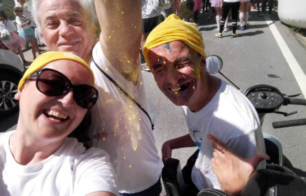 Três pessoas, sorridentes, fazem uma “selfie”. Vê-se pó amarelo a ser espalhado.