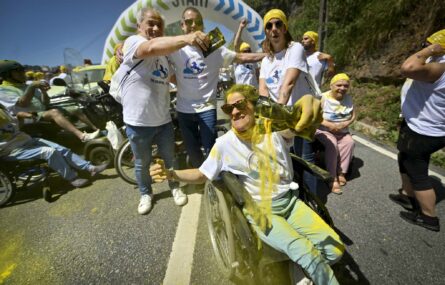 Várias pessoas alinhadas junto ao ponto de partida da corrida. Estão parcialmente cobertas de pó colorido (essencialmente amarelo).