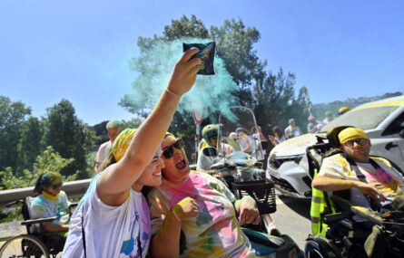 Várias pessoas durante a corrida. Uma delas espalha o pó azul de saco que leva na mão. Ao fundo da imagem mais participantes e inúmeras árvores.