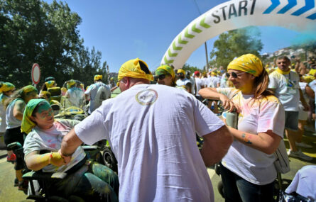 Várias pessoas alinhadas junto ao ponto de partida da corrida. Estão parcialmente cobertas de pó colorido.
