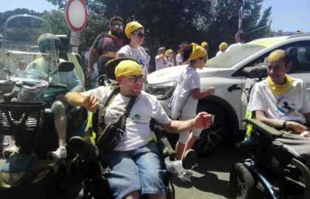 Várias pessoas alinhadas junto ao ponto de partida da corrida. Estão parcialmente cobertas de pó colorido. Ao fundo vê-se, parcialmente, uma das viaturas de apoio da prova.