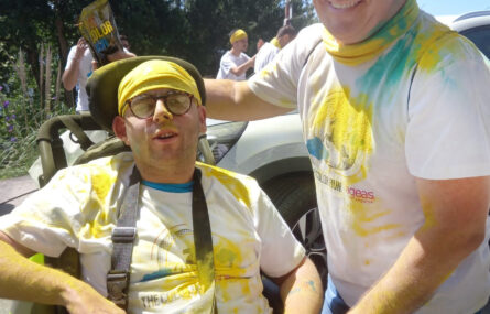 Duas pessoas sorridentes e cobertas de pó colorido (azul e amarelo).