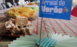 Fotografia de uma mesa com cartão a identificar o Arraial de verão de 28 de julho. Na mesa são visíveis alguns pratos com comida.
