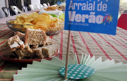 Fotografia de uma mesa com cartão a identificar o Arraial de verão de 28 de julho. Na mesa são visíveis alguns pratos com comida.