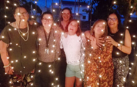 Seis pessoas fazem retrato sendo que à frente delas estão penduradas algumas fileiras com pequenas luzes.