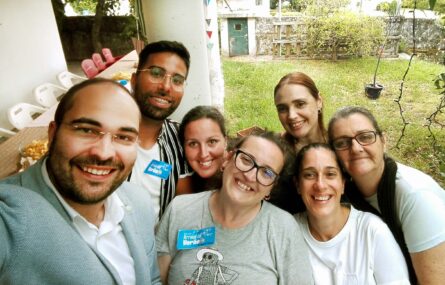 Sete pessoas sorriem para a fotografia. Ao fundo vê-se a relva do jardim e alguns pequenos arbustos.