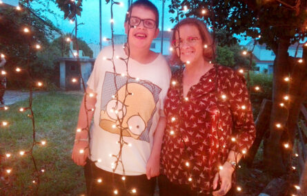 Duas pessoas fazem retrato sendo que à frente delas estão penduradas algumas fileiras com pequenas luzes.