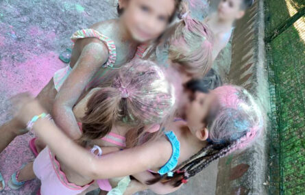 Grupo de seis crianças, em fato de banho, cheias de pó colorido (de várias cores). Todos os rostos das crianças foram desfocados.