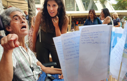António Magalhães junto de uma pessoa com a qual conversa. Ao fundo mais pessoas e vários stands de venda de livros. Em primeiro plano algumas folhas de papel com mensagens e dedicatórias de pessoas que compraram o livro.