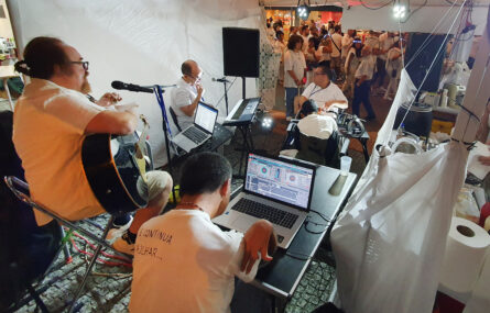 Fotografia feita na parte de trás do pequeno palco improvisado para as atuações da “appSound” e do DJ ET. Além dos equipamentos (da banda e do DJ), ao fundo distinguem-se pessoas a assistir.