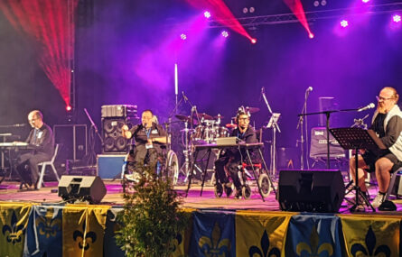 Plano mais aproximado dos quatro elementos da banda appSound em palco. Iluminação do palco em tons roxo e vermelho.