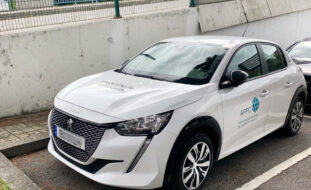 Fotografia, em perspetiva diagonal, de um carro estacionado. A viatura é de marca Peugeot e de cor branca. Na porta lateral, do condutor, vê-se o logótipo da APPC e a designação da instituição: Associação do Porto de Paralisia Cerebral. Atrás do referido carro ainda se consegue ver um pouco de outra viatura.
