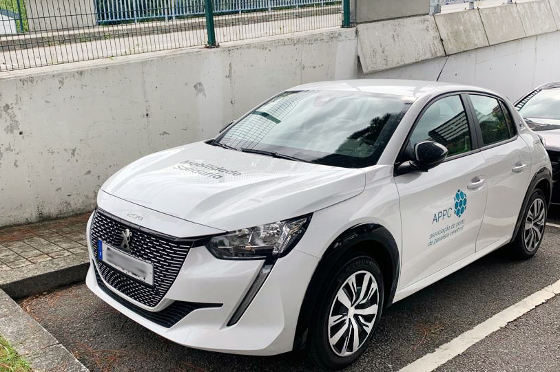 Fotografia, em perspetiva diagonal, de um carro estacionado. A viatura é de marca Peugeot e de cor branca. Na porta lateral, do condutor, vê-se o logótipo da APPC e a designação da instituição: Associação do Porto de Paralisia Cerebral. Atrás do referido carro ainda se consegue ver um pouco de outra viatura.