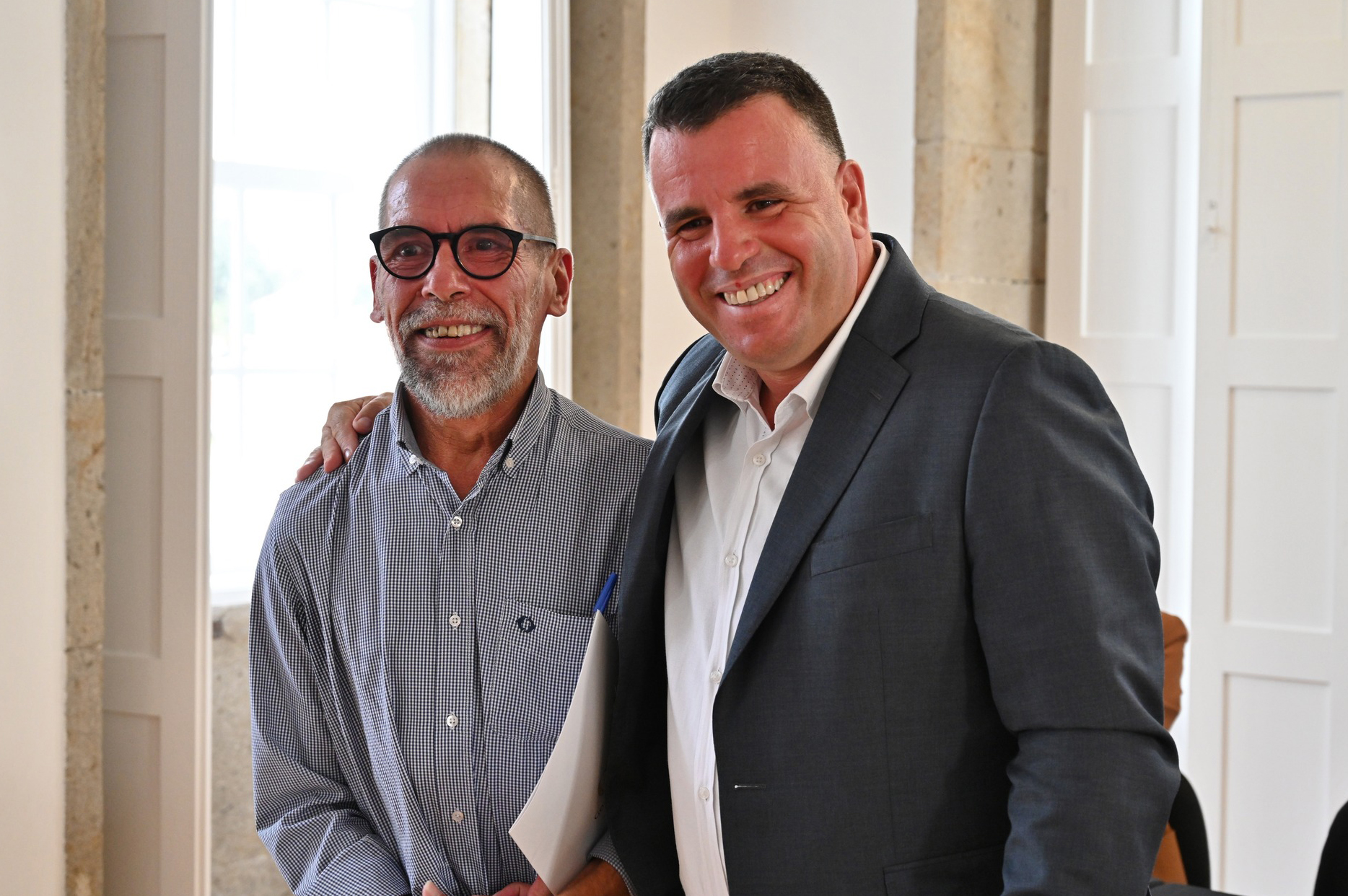 Fotografia de duas pessoas sorridentes, sendo que uma delas coloca o braço por cima do ombro da outra. Na imagem, à esquerda, está Abílio Cunha, presidente da Associação do Porto de Paralisia Cerebral. À direita surge Marco Martins, presidente da Câmara Municipal de Gondomar.