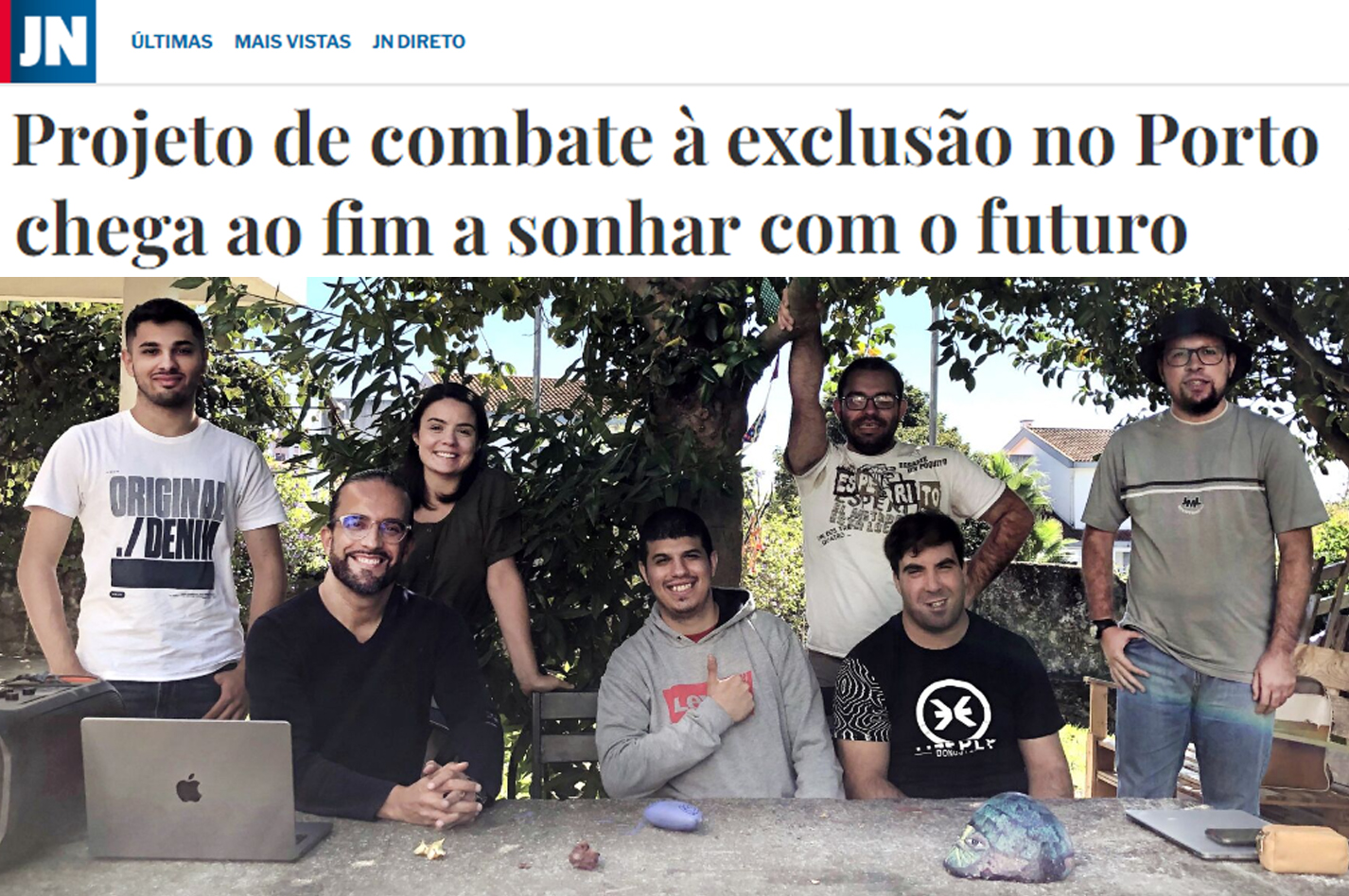 Cópia parcial de notícia publicada no sítio do Jornal de Notícias. Em cima barra com logótipo do JN. Depois título da notícia “Projeto de combate à exclusão no Porto chega ao fim a sonhar com o futuro” e logo abaixo fotografia de sete pessoas (de pé e sentadas) junto da uma mesa de pedra de um jardim. Em cima da mesa está pousado um computador portátil. Atrás das pessoas uma árvore e alguns arbustos.
