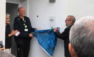 Duas pessoas retiram uma bandeira, da APPC, que cobria uma placa (com a indicação IVD). Mais à esquerda vê-se, parcialmente, uma terceira pessoa – igualmente sorridente.
