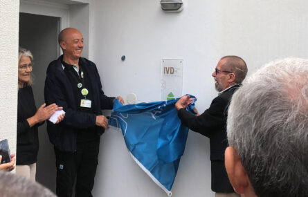 Duas pessoas retiram uma bandeira, da APPC, que cobria uma placa (com a indicação IVD). Mais à esquerda vê-se, parcialmente, uma terceira pessoa – igualmente sorridente.