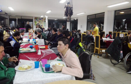 Fotografia do refeitório da Villa Urbana da APPC. Mesa gigante em forma de U com perto de três dezenas de pessoas sentadas, a comer.
