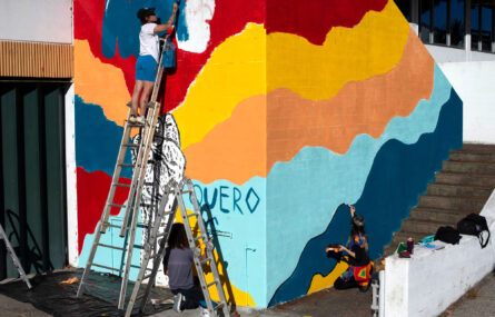 Parede do Centro de Reabilitação a ser pintada. Uma pessoa está num escadote, pintando as letras onde diz “APPC”. Outra pessoa está de joelhos, por baixo do escadote, a pintar. Outra pessoa está de lado também a pintar.