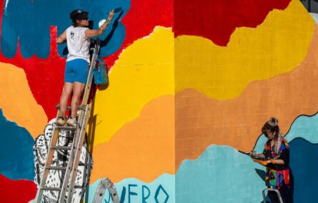 Parede do Centro de Reabilitação a ser pintada. Uma pessoa está no escadote a pintar as letras da palavra “APPC”. Outra está de pé, na zona lateral, a retocar uma parte do desenho.