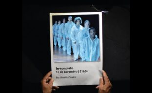 Fotografia, em plano superior de duas mãos a segurarem um cartaz. Acima do cartaz surge a indicação do 42.º Encontro de Teatro de Os Plebeus Avintenses. O cartaz é composto de uma fotografia de sete atores vestidos com roupas integralmente brancas e alinhados, em fila. Depois, logo abaixo, surge o nome da peça (IN-completo), data e hora de apresentação (10 de novembro às 21h30) e o nome da companhia (Era uma vez Teatro).